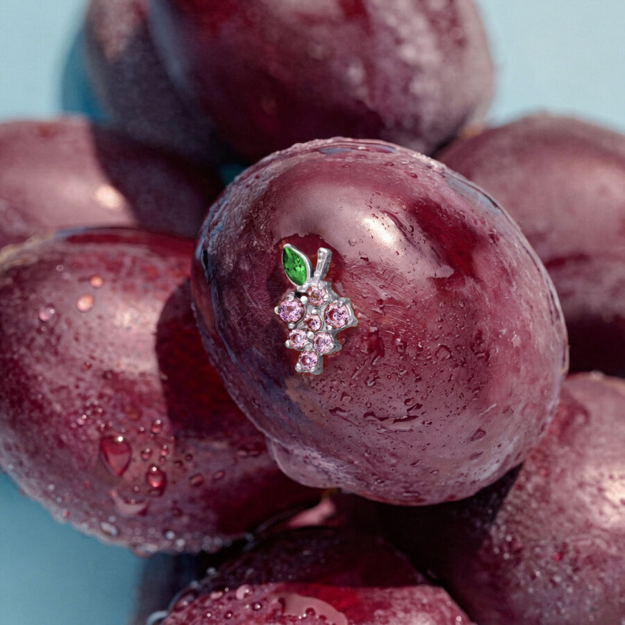 Ajuste de uvas plateadas con hojas verdes sobre ciruela morada, rodeado de más ciruelas sobre fondo azul