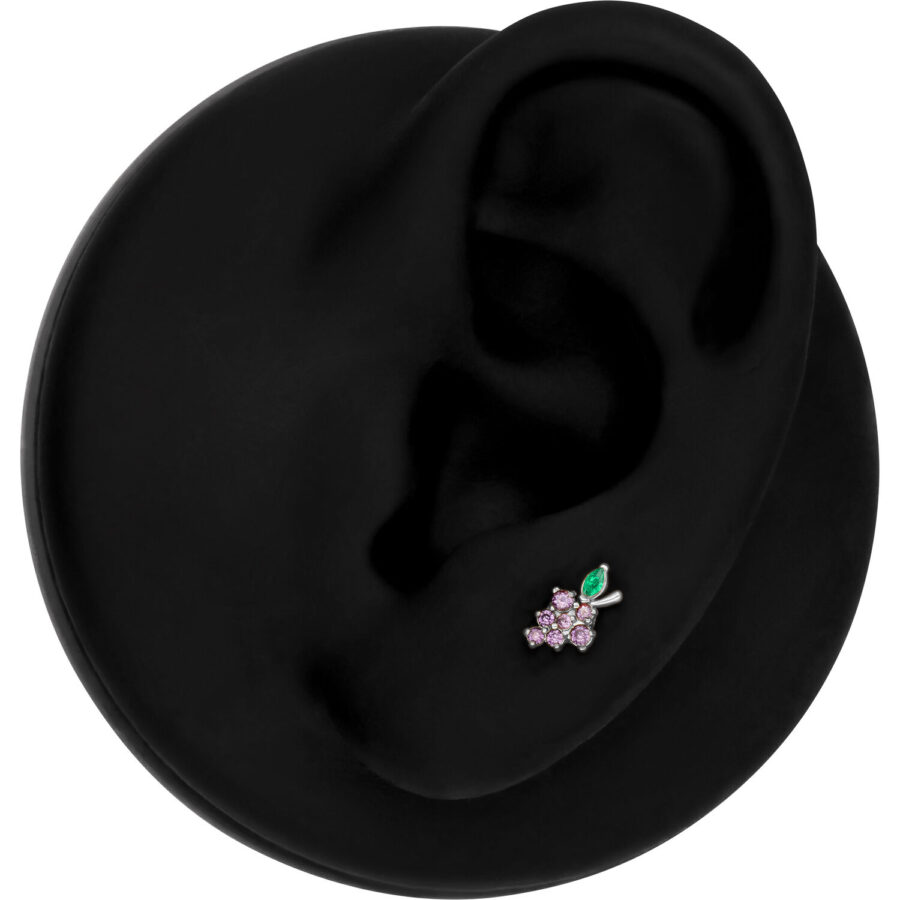 Accesorio de piercing plateado en forma de uva con piedras moradas y verdes en un modelo de oreja negra