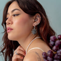 Ajuste a presión de uva plateada Mujer con varios piercings plateados en la oreja, lleva un collar de perlas y sostiene uvas.