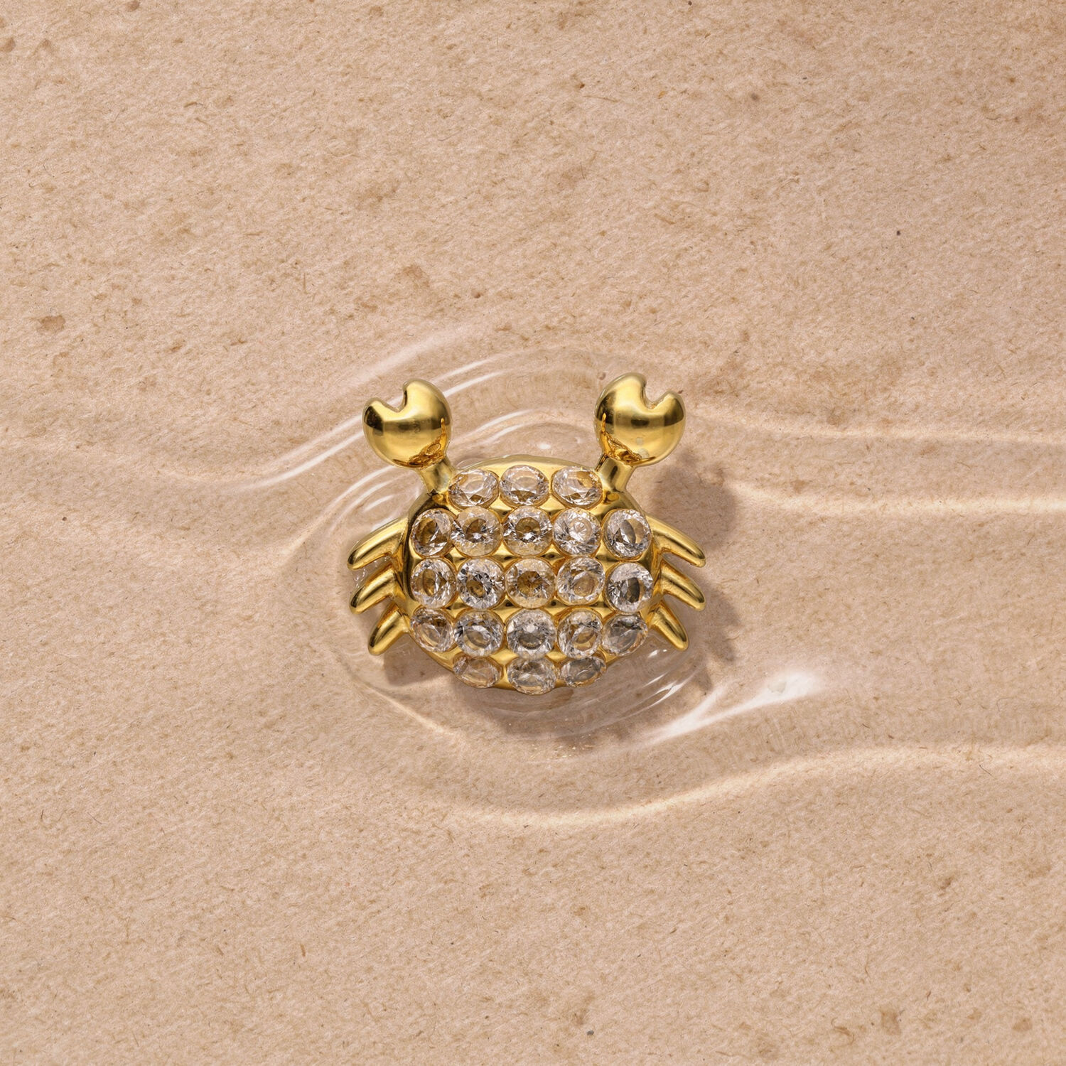 Adorno dorado de cangrejo con piedras de strass sobre fondo arenoso