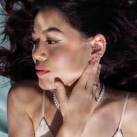 Mujer con accesorios de piercing dorados en la oreja, mano en la cara, acostada