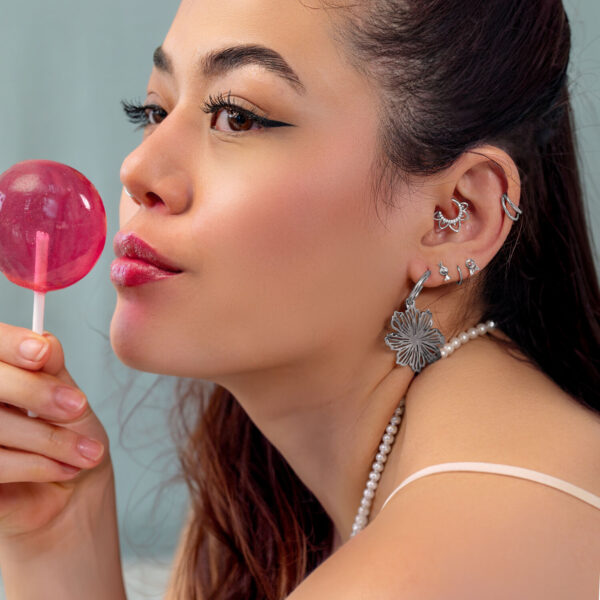 Mujer con varios piercings de oreja plateados y un Lollipop rosa, de lado