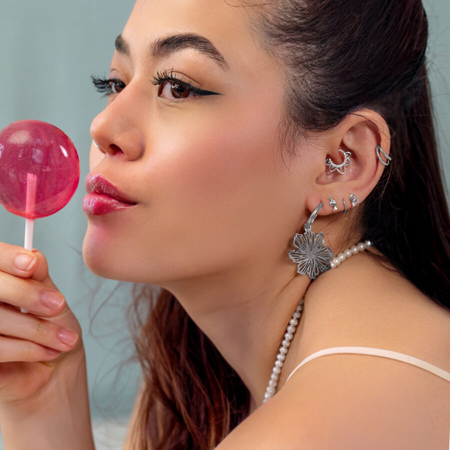 Mujer con varios piercings de oreja plateados y un Lollipop rosa, de lado