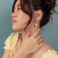 Pendientes y anillos dorados en mujer Mujer con pendientes y anillos dorados, camiseta amarilla, fondo azul