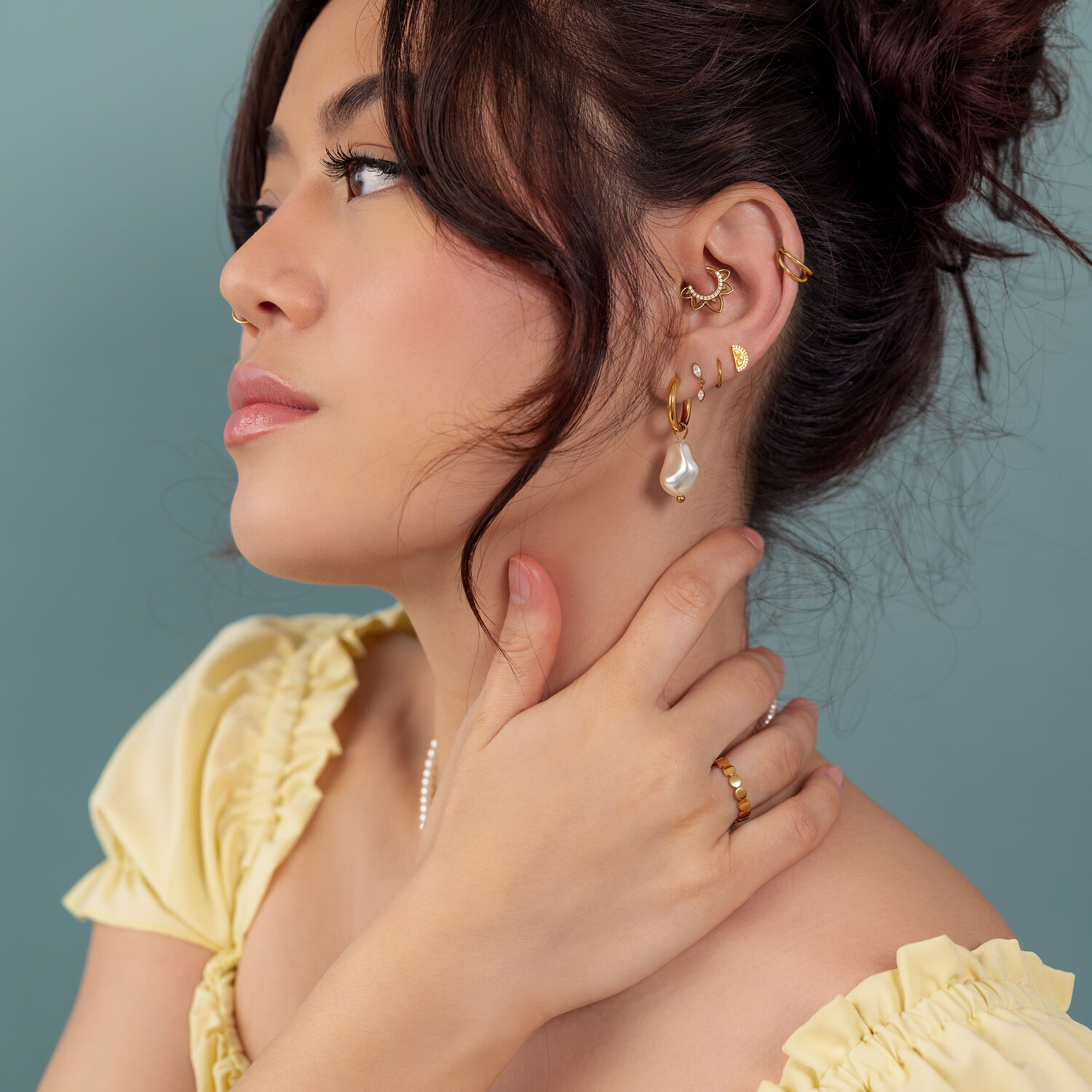 Pendientes y anillos dorados en mujer Mujer con pendientes y anillos dorados, camiseta amarilla, fondo azul