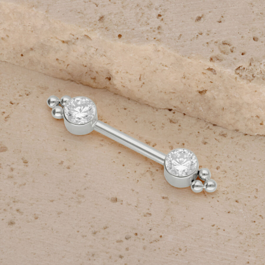 Barra de titanio de oro blanco con dos circonitas sobre fondo arenoso