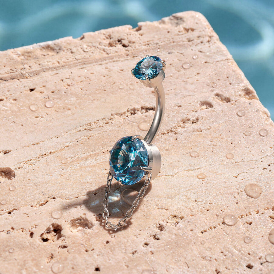 Piercing de ombligo con cristales turquesa y cadena sobre piedra