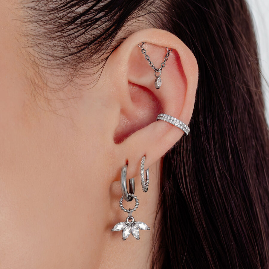 Primer plano de una oreja con varios pendientes plateados, incluido un colgante de abanico con cristales.
