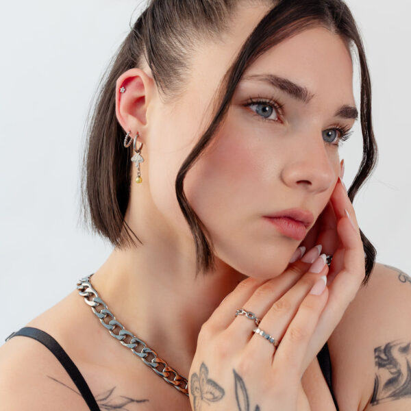Mujer con pelo corto lleva pendientes de plata y oro en forma de seta y un collar, sobre fondo blanco