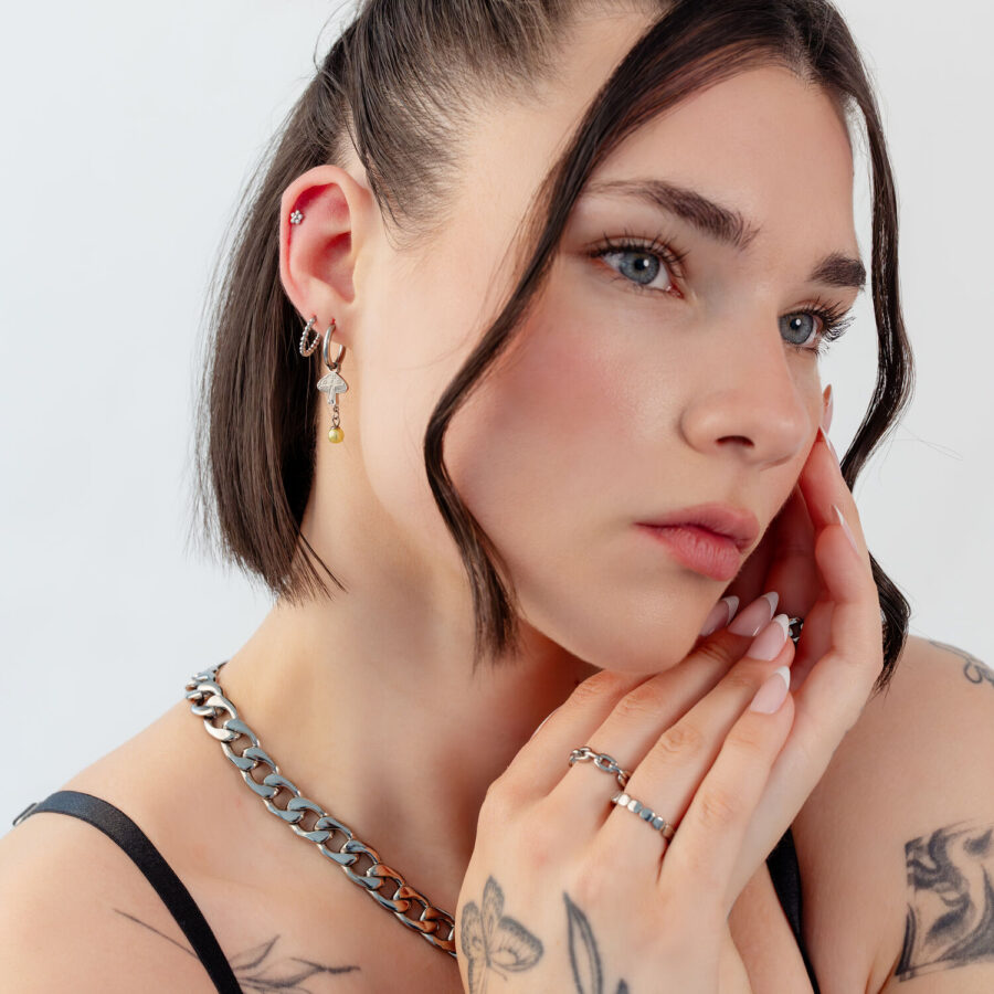 Mujer con pelo corto lleva pendientes de plata y oro en forma de seta y un collar, sobre fondo blanco