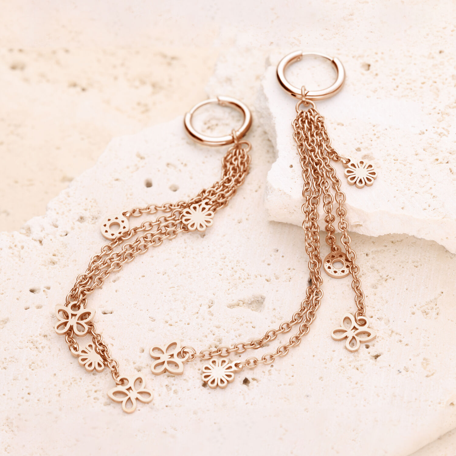 Creolen de oro rosa con cadenas largas y colgantes de flores sobre piedra clara