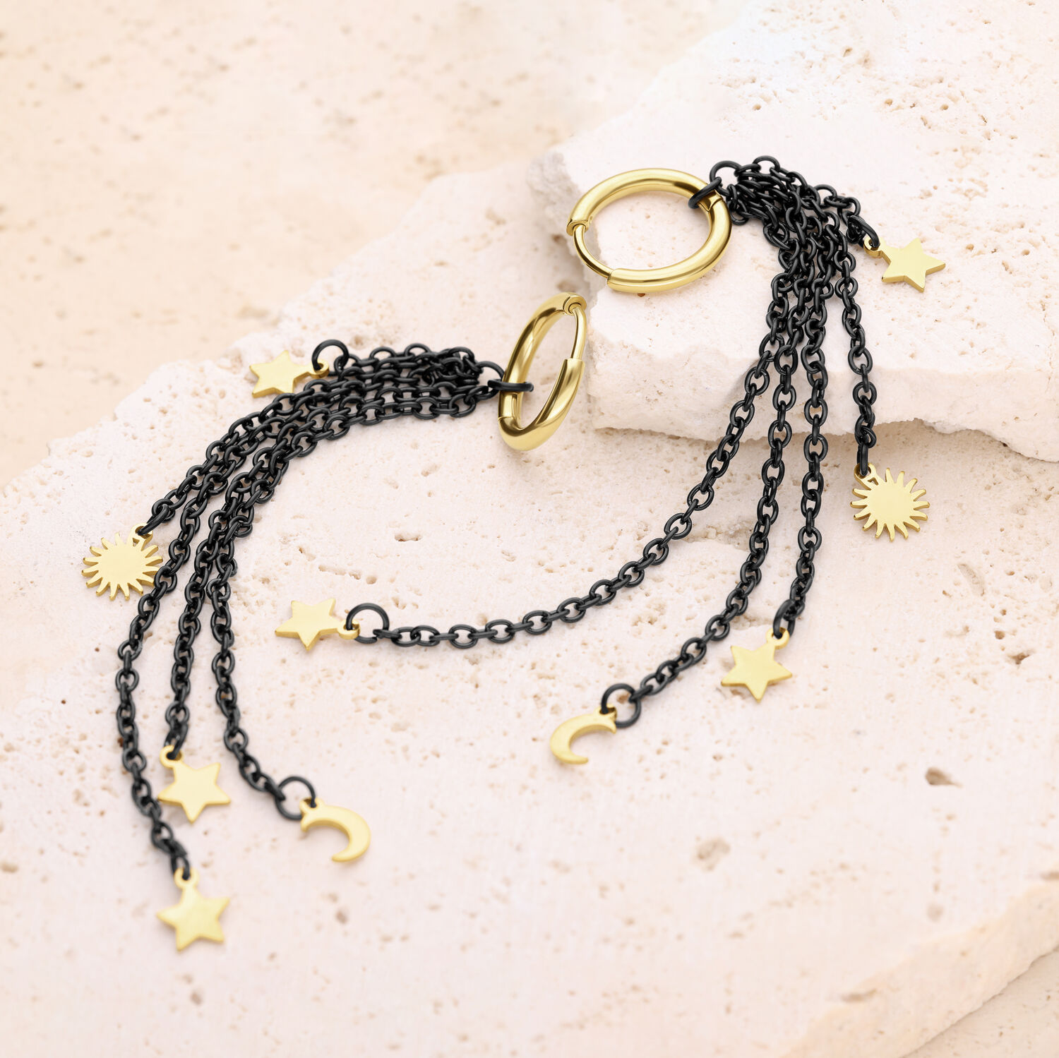 Pendientes Colgantes Mystic Night Oro/Negro Pendientes negros y dorados con colgantes de estrellas y lunas sobre un fondo beige
