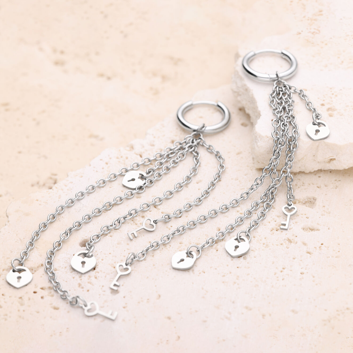 Pendientes plateados con colgantes de cadena Aros plateados con largas cadenas y motivos de corazón y llave sobre fondo de piedra clara