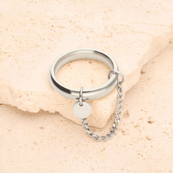 Anillo de plata con pequeña cadena y colgante redondo sobre piedra clara