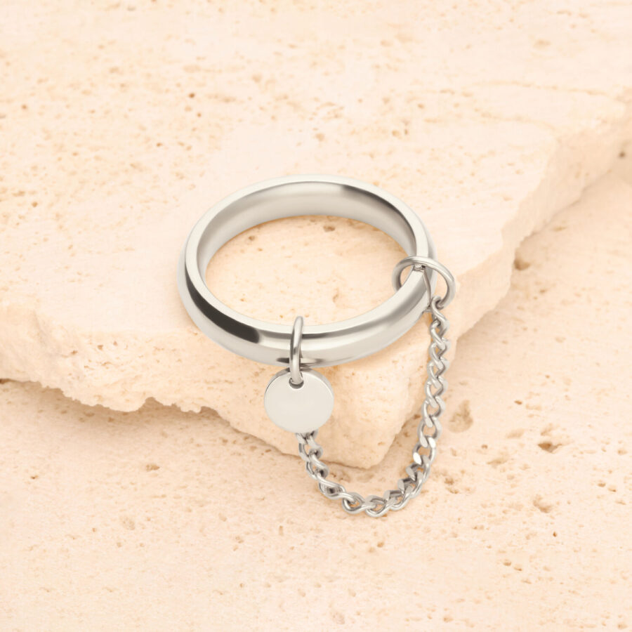 Anillo de plata con pequeña cadena y colgante redondo sobre piedra clara