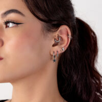 Primer plano de una oreja humana con varios piercings plateados, incluido un colgante de estrella, sobre un fondo blanco.