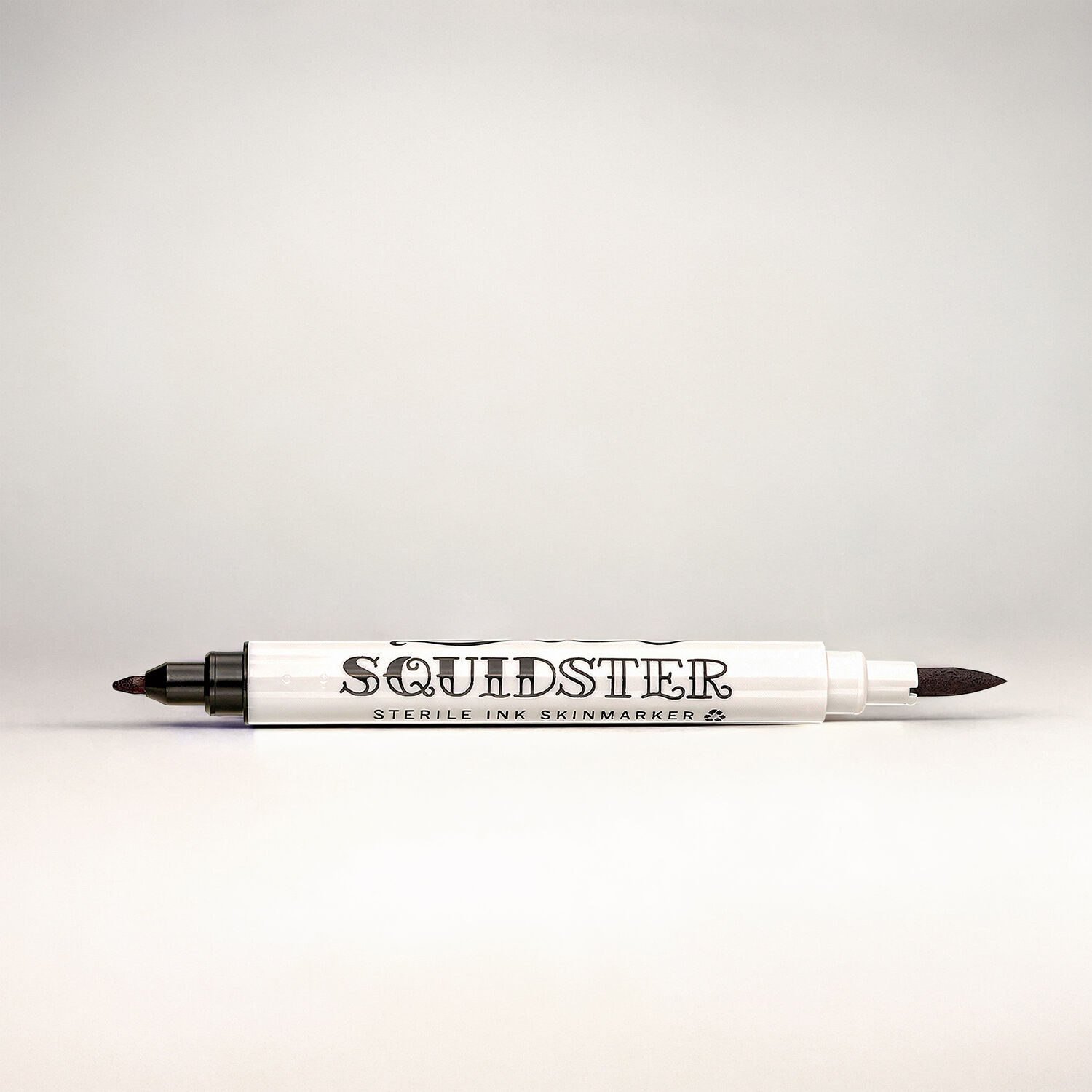 Marcador de Tatuajes Squidster Negro Marcador de tatuajes blanco con dos puntas negras sobre fondo gris