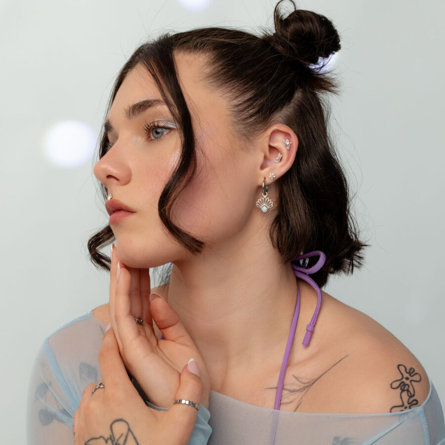 Mujer con cabello oscuro lleva un piercing de oreja dorado y blanco en forma de flores de jazmín con ópalo, sobre un fondo claro