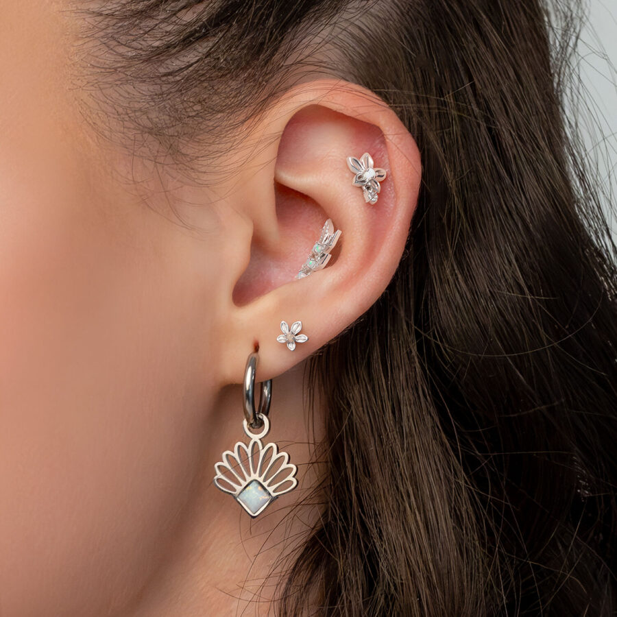 Primer plano de una oreja con varios pendientes y piercings en forma de flores de jazmín de titanio, sobre fondo blanco