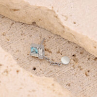 Pendiente de plata con colgante de cadena Pendiente de plata con piedra cuadrada cristalina y colgante de cadena sobre piedra beige.