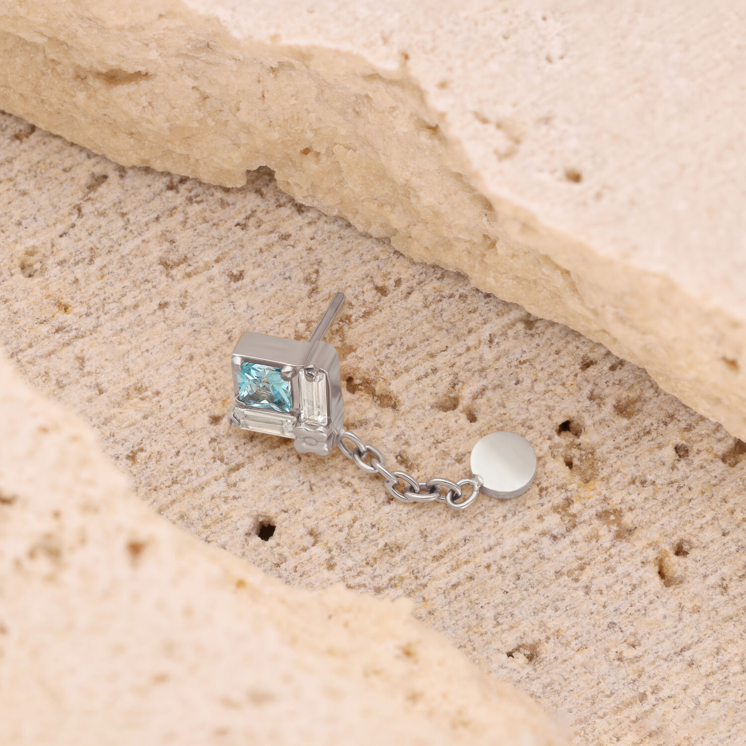 Pendiente de plata con colgante de cadena Pendiente de plata con piedra cuadrada cristalina y colgante de cadena sobre piedra beige.
