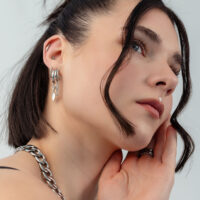 Pendientes de plata con cadena y adorno Primer plano de una mujer con cabello oscuro que lleva pendientes de plata con cadenas y un adorno semióvalo.
