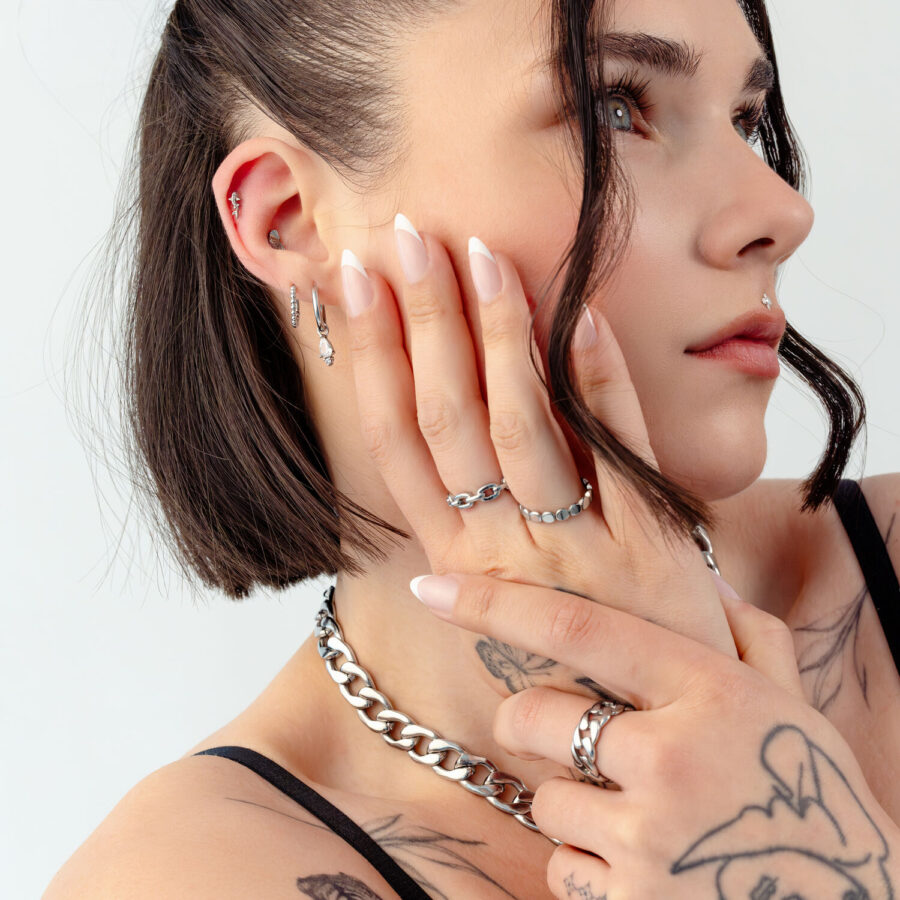 Mujer con pelo corto, tatuajes y varias joyas de plata sobre fondo blanco