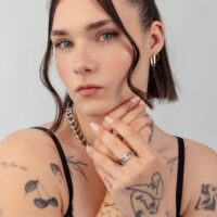 Mujer con cabello corto lleva cadena y pendientes plateados, tatuajes visibles