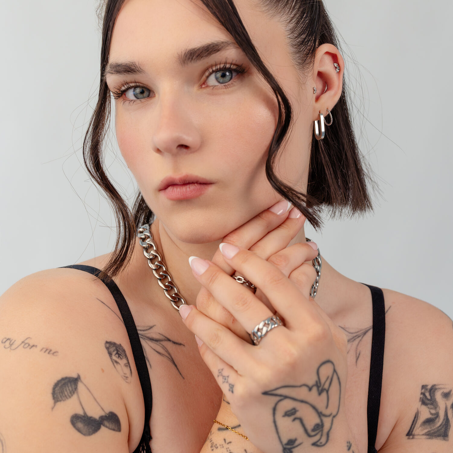 Mujer con cabello corto lleva cadena y pendientes plateados, tatuajes visibles