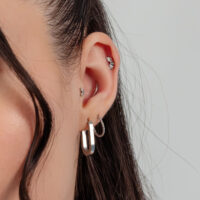 Primer plano de una oreja con pendientes de plata y un accesorio de piercing de rayos de sol plegados.