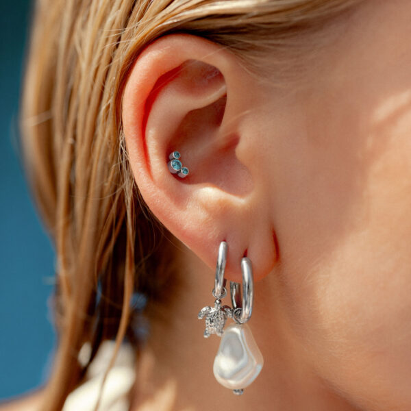 Oreja con aros plateados y adorno de cristal turquesa, primer plano
