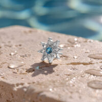 Aqua Bloom Adorno de Cristal Turquesa Adorno plateado con cristal turquesa sobre superficie de piedra mojada frente a un fondo de piscina desenfocado