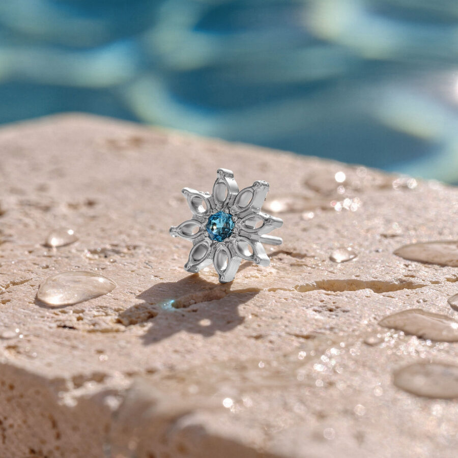 Adorno plateado con cristal turquesa sobre superficie de piedra mojada frente a un fondo de piscina desenfocado