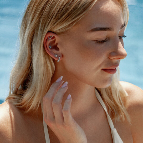 Mujer con varios pendientes, incluido un pendiente de oro blanco con cristal turquesa, sobre fondo azul