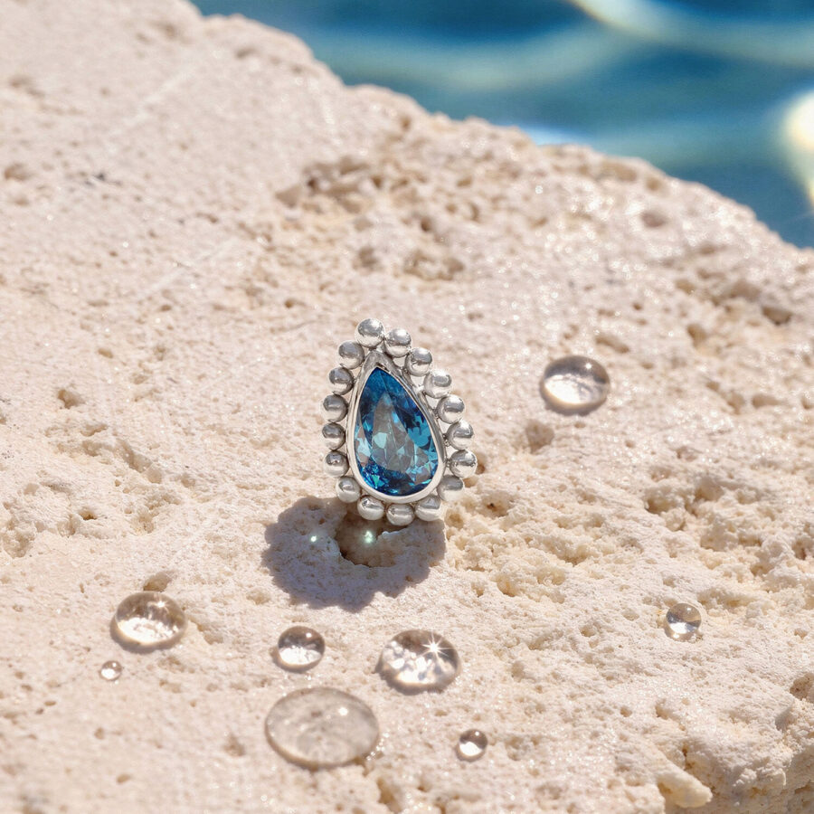 Ajuste de cristal turquesa sobre superficie de piedra clara con gotas de agua