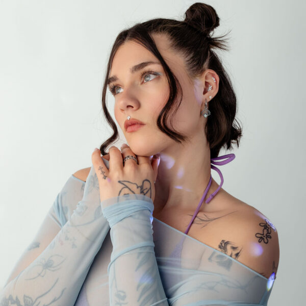 Mujer con top de malla azul y patrón de tatuaje sobre fondo blanco