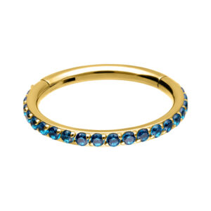Clicker de piercing dorado con cristales turquesas, dispuestos alrededor sobre fondo blanco.
