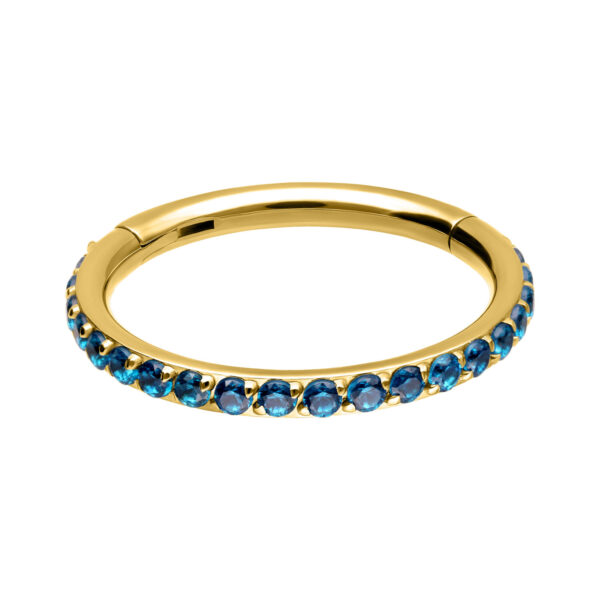 Clicker de piercing dorado con cristales turquesas, dispuestos alrededor sobre fondo blanco.