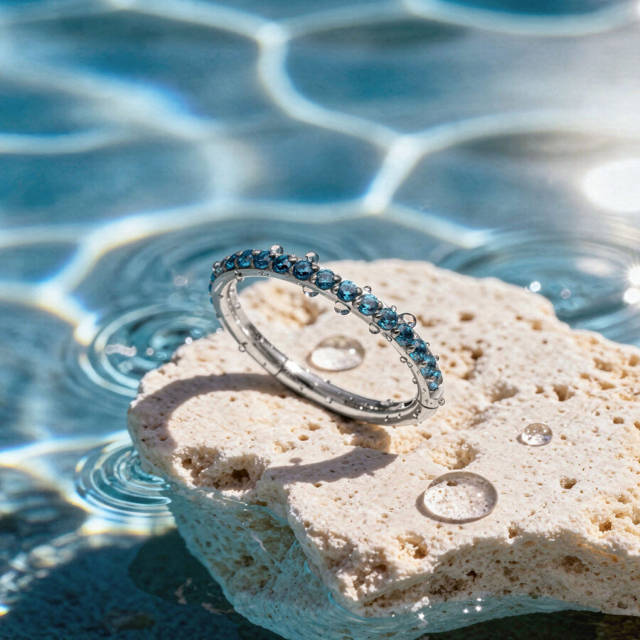 Anillo de cristal turquesa sobre una piedra clara al borde de una piscina con reflejos de luz solar