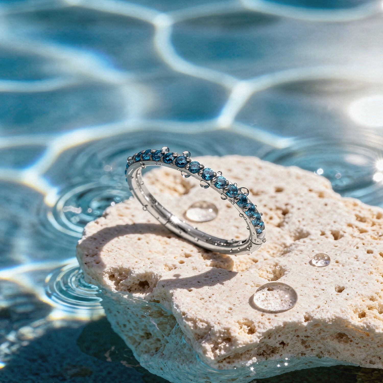 Anillo de cristal turquesa sobre piedra Anillo de cristal turquesa sobre una piedra clara al borde de una piscina con reflejos de luz solar
