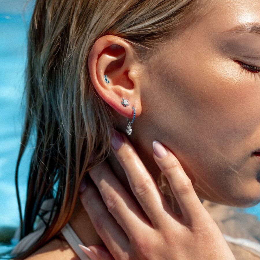 Mujer con varios piercings en la oreja, incluyendo un clicker de cristal turquesa, en la piscina