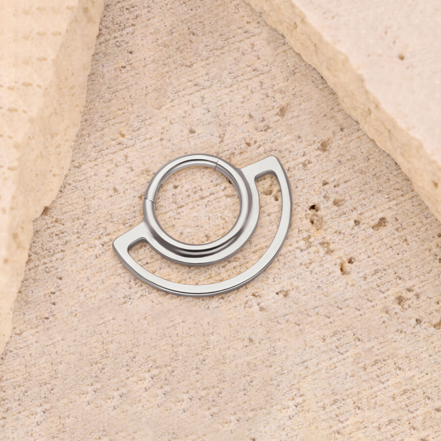 Clicker de anillo plateado sobre fondo de piedra beige, diseño circular