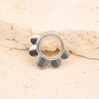 Clicker Half Flower plateado frente a una piedra beige sobre fondo claro