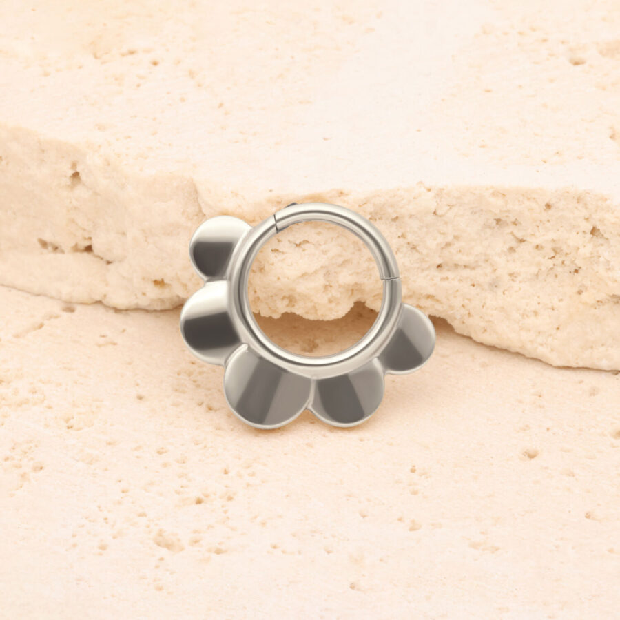 Clicker Half Flower plateado frente a una piedra beige sobre fondo claro