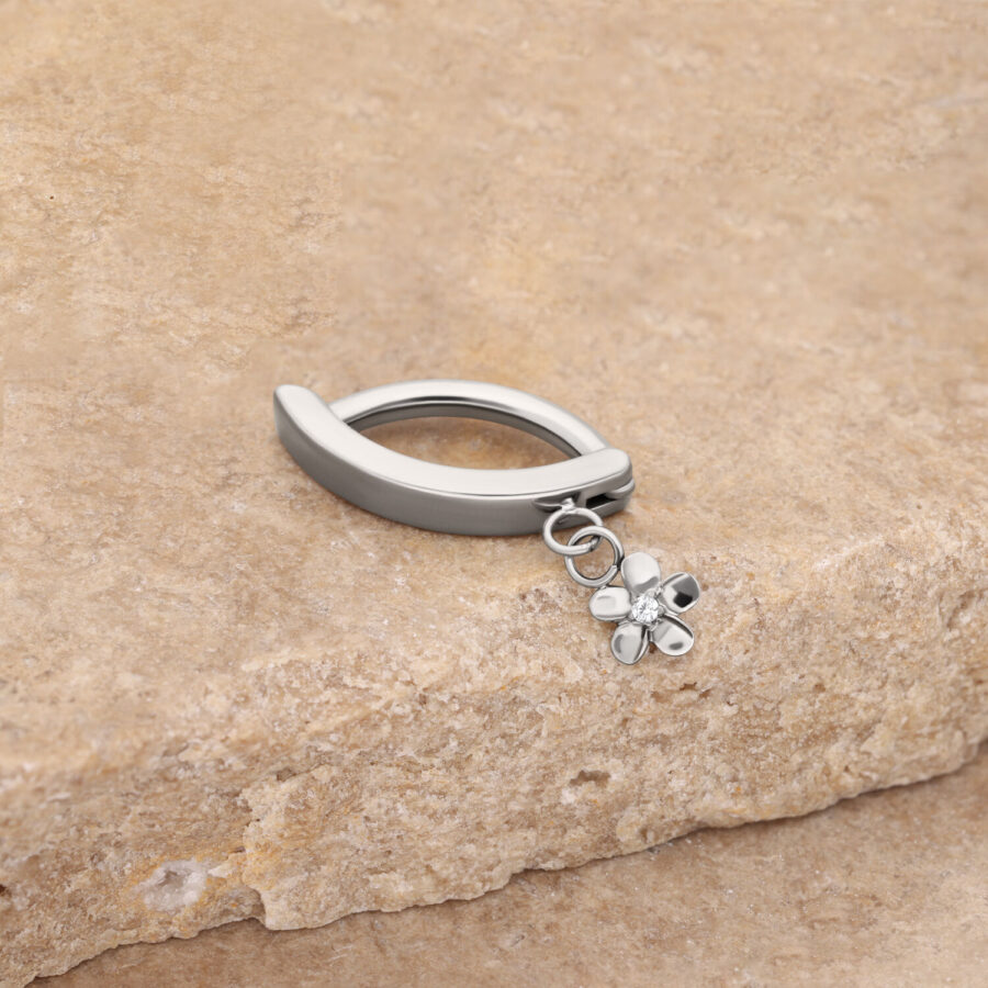 Anillo de ombligo plateado con colgante de flor sobre fondo de piedra