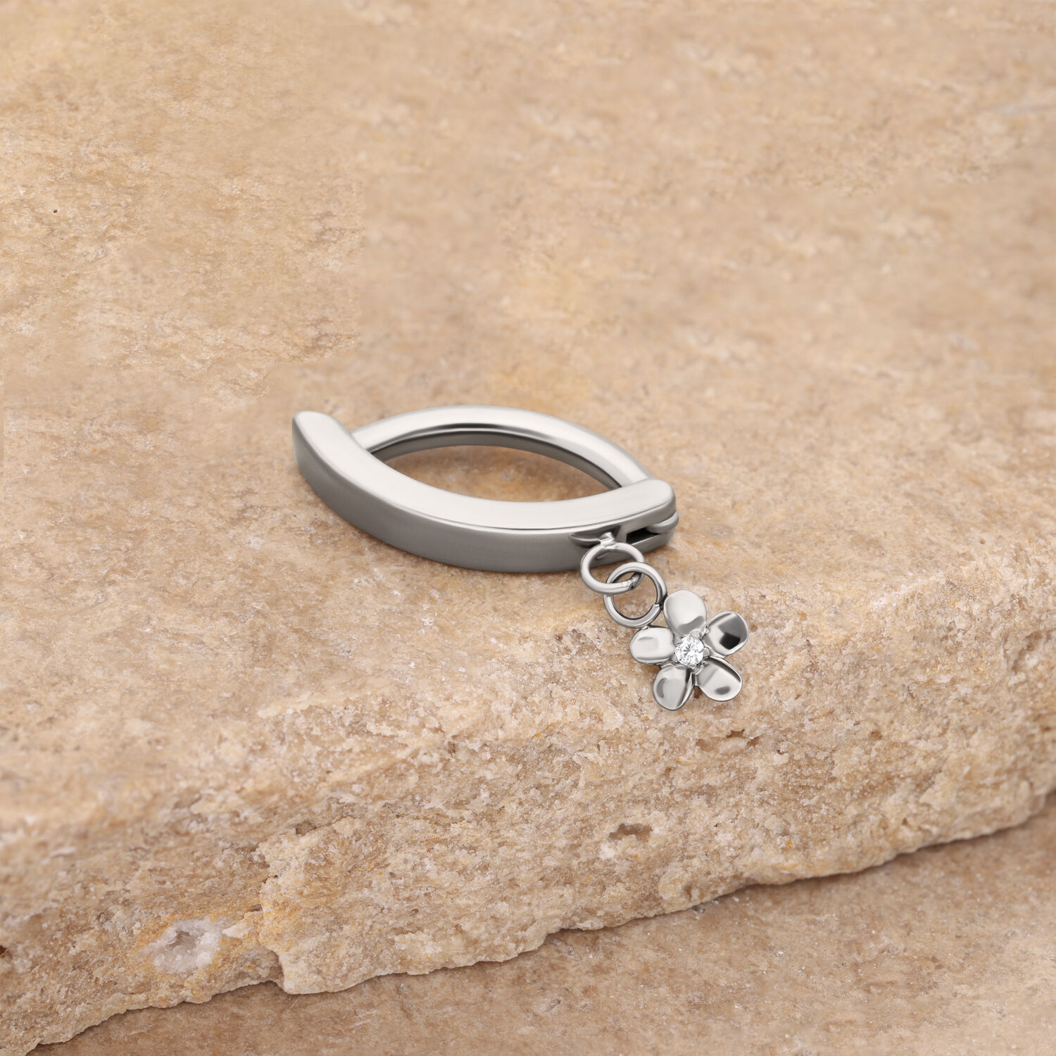 Clicker de ombligo plateado con colgante de flor Anillo de ombligo plateado con colgante de flor sobre fondo de piedra