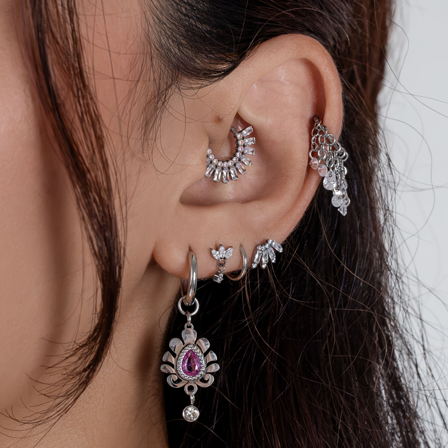 Combinación de joyas de oreja plateadas con cristales Varios pendientes plateados con cristales en una oreja, primer plano