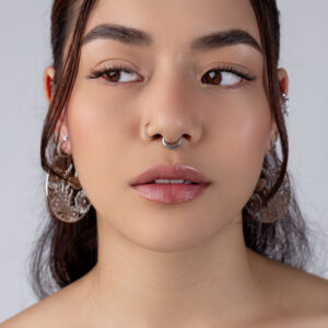 Primer plano de un rostro con septum clicker plateado y grandes pendientes