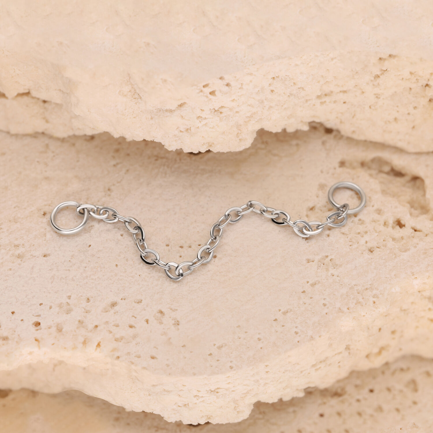 Cadena de piercing plateada 15 mm Cadena de piercing plateada con anillos sobre fondo de piedra beige