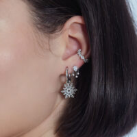 Elegante colgante de cristal para piercing de oreja Colgante de cristal plateado en la oreja con otros piercings sobre fondo blanco